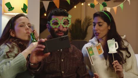 grupo de amigos disfrazándose con novedades irlandesas y accesorios en casa o en el bar posando para selfies celebrando en la fiesta del día de san patricio