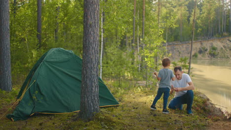 the boy helps his father to set up and assemble a tent in the forest. teaching children and travelling together in a tent camp