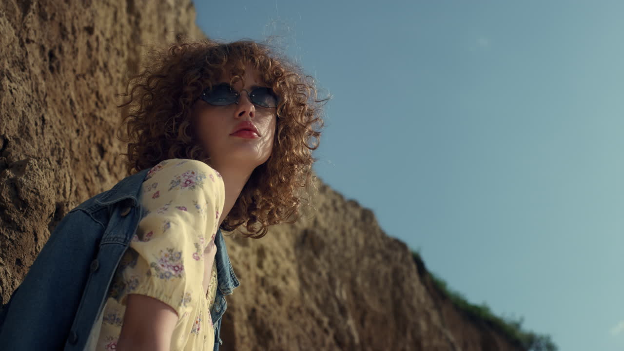 힐 근처에 서 있는 카메라를 내려다보고 있는 편안한 소녀. 포즈를 취하는 여자.