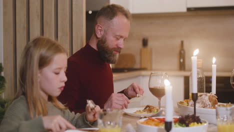 camera focuses a father and daughter having dinner at christmas sitting at the table and talking with other family members