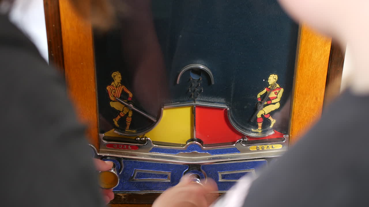 A machine with a vintage football or cricket theme penny arcade game interface is being played by two players turning a dial. Retro arcade game early pinball 19th century early 20th century