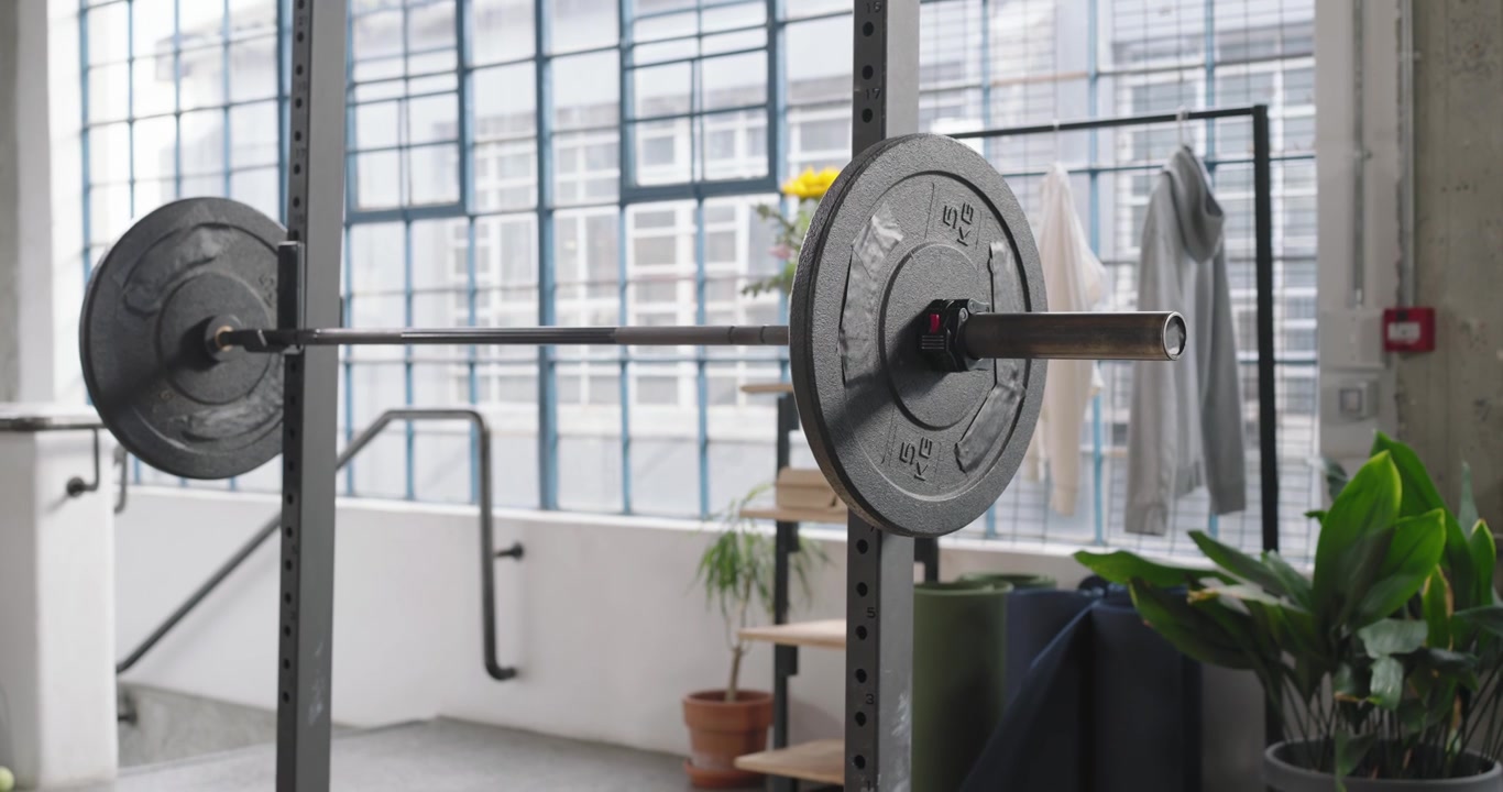 Camera is panning and lowering to showcase mounted barbell with large right plate in loft space