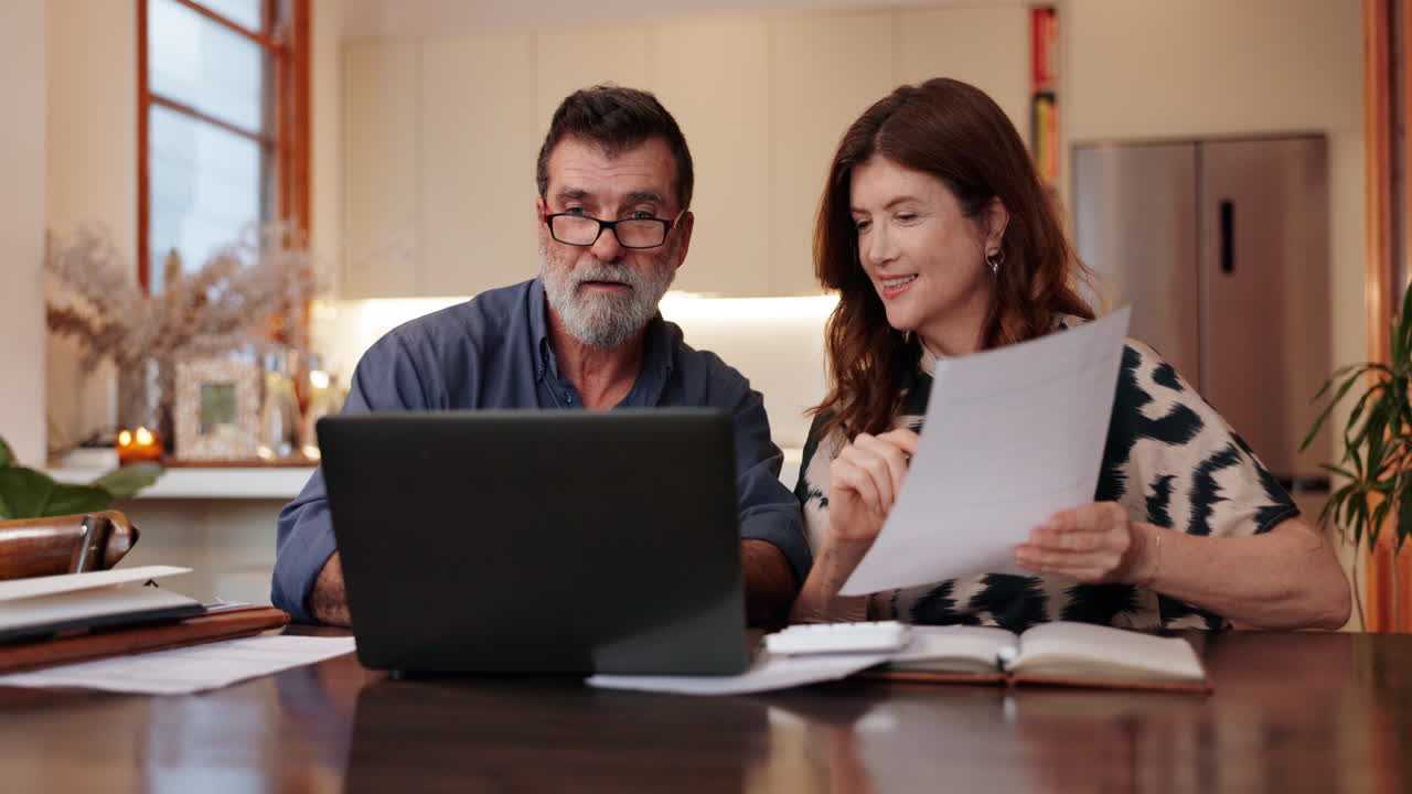 pareja revisando documentos en la computadora portátil en la cocina
