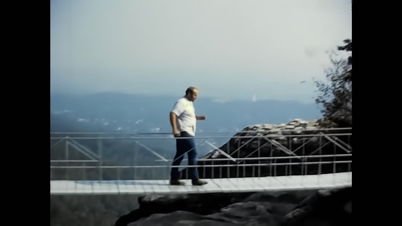 Man Stands on Bridge With Hands Up, Vintage Capturing 1970s Era in the USA. CIRCA USA - 1970s: A vintage video from the 1970s in the USA, showing a man standing on a bridge with his hands raised.