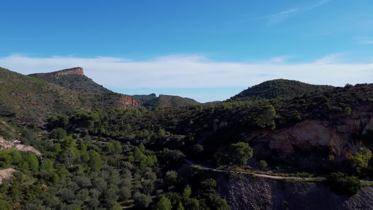 4K drone slow ascent revealing a panoramic view of arid Mediterranean mountains, featuring exposed rocky cliffs and dense pine forest in Valencia, Spain, under a clear blue sky