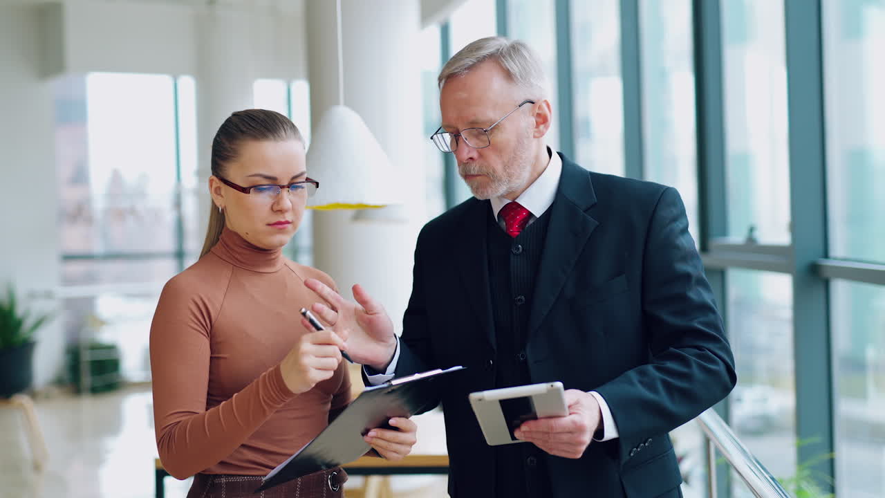 Il capo dà una penna a un'assistente donna per firmare dei documenti in ufficio con grandi finestre con vista sulla città. Video con persone d'affari.
