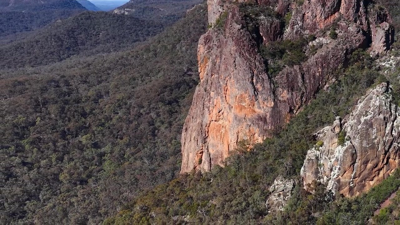Inquadratura ampia di formazione rocciosa di dicco vulcanico e catena montuosa nel Parco Nazionale Warrumbungle, Australia.