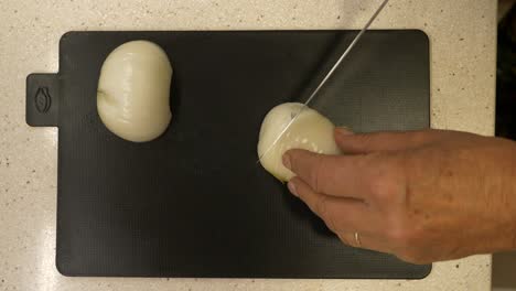 slicing white onions with a stainless steel knife on a black chopping board - top view