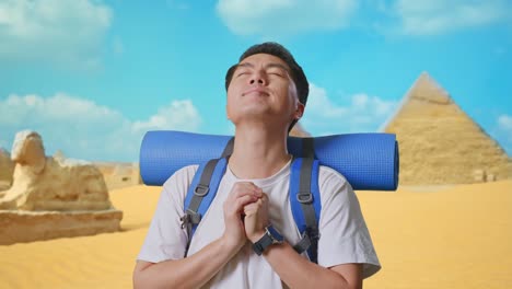 close up of asian male hiker with mountaineering backpack pray for something while traveling in pyramid of giza