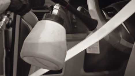 ingeniero profesional con guantes negros usando hábilmente una pistola de tornado para limpiar el cinturón de seguridad del coche