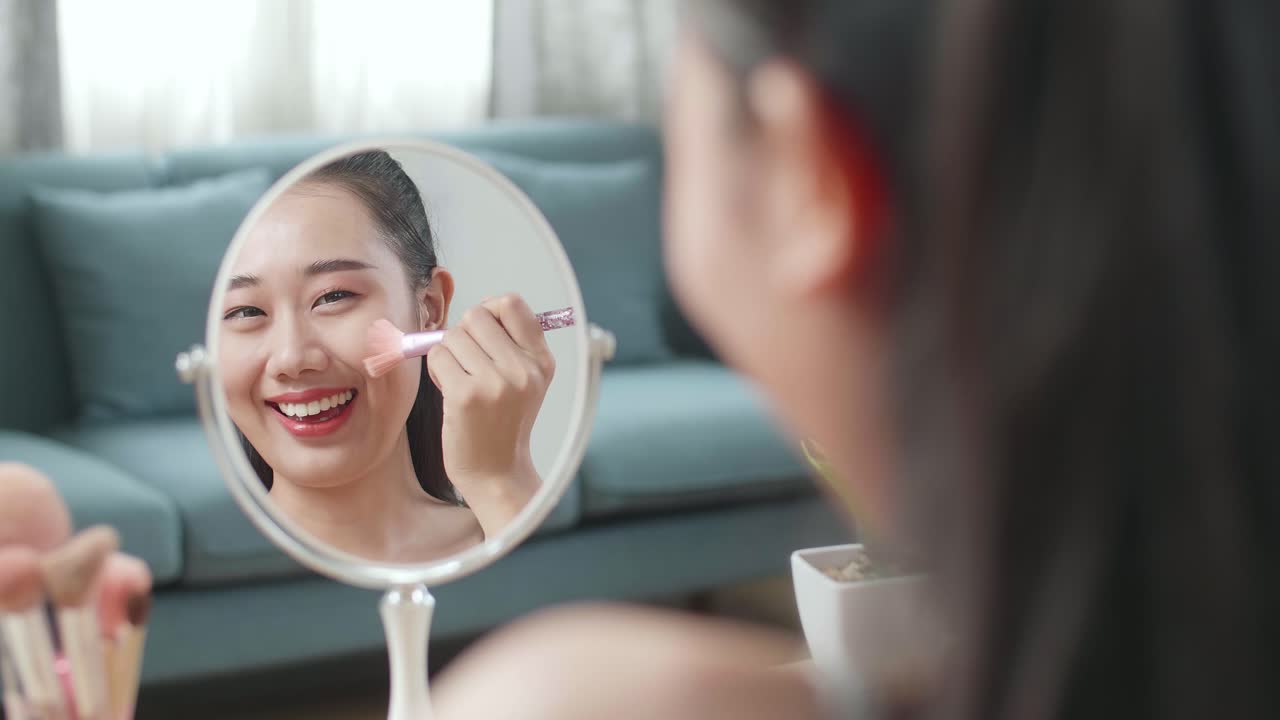 Reflection In A Mirror Beautiful Young Asian Woman Rouging Her Cheeks And Smiling While Applying Makeup At Home