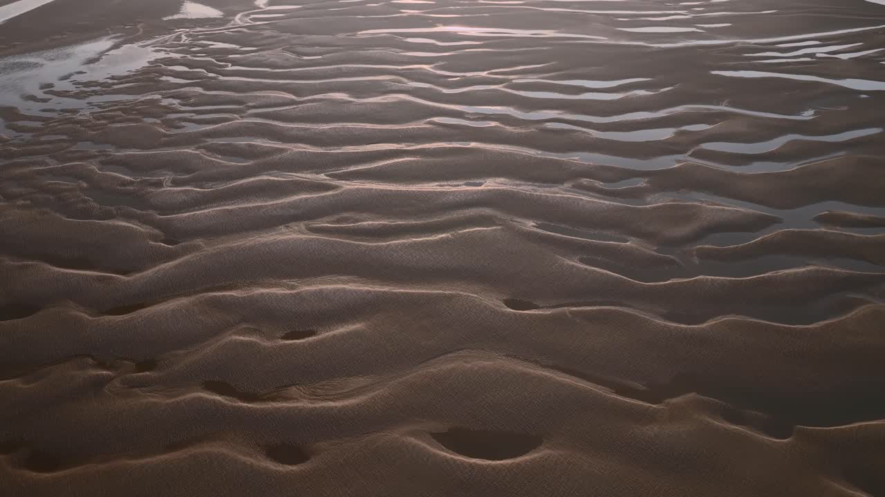 Undulating sand patterns and seawater pools at sunset. Slow flight aerial footage.