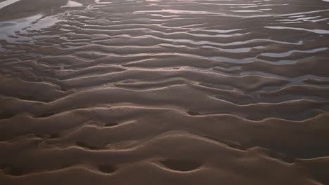 undulating sand patterns and seawater pools at sunset. slow flight aerial footage.