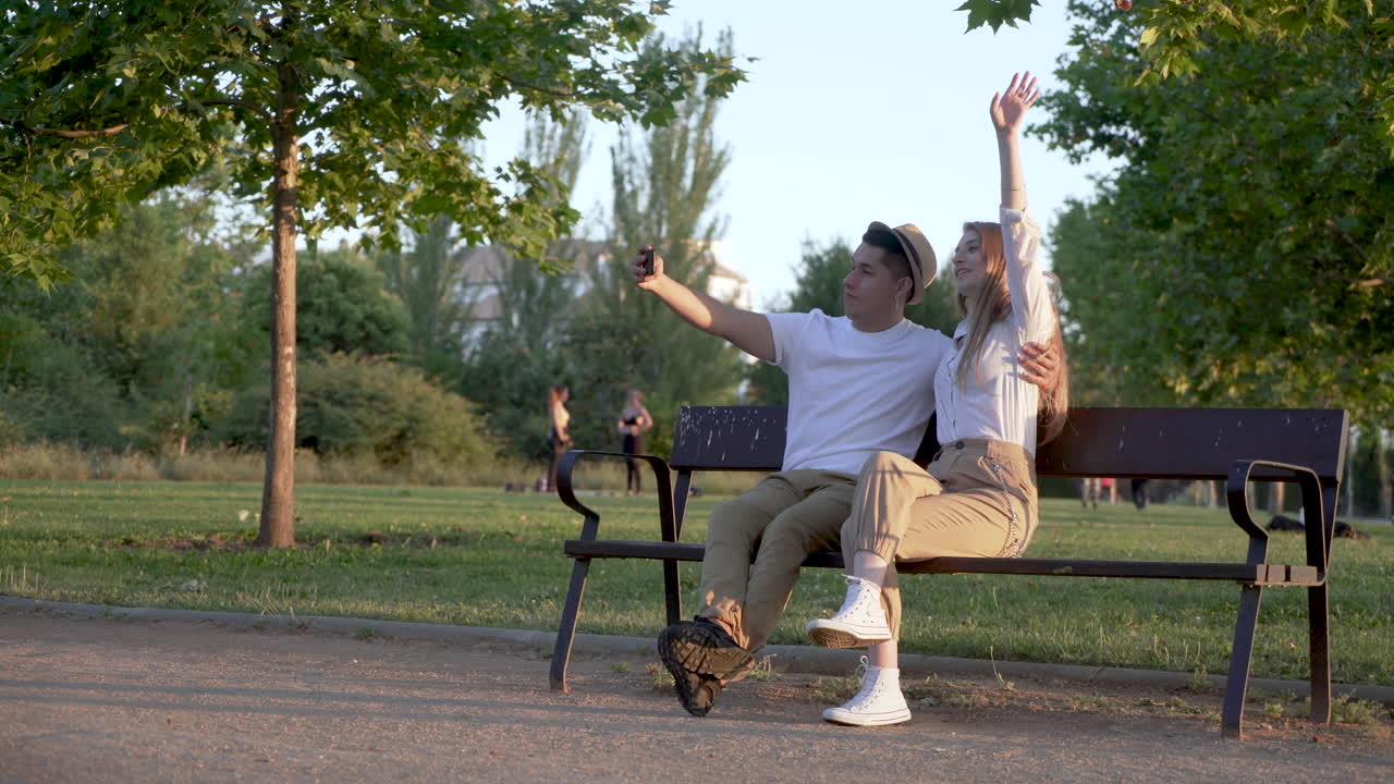 Young couple taking a selfie on their mobile sitting in the park. Latin man and Caucasian woman