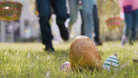 close up of children running to pick up chocolate egg on easter egg hunt in garden