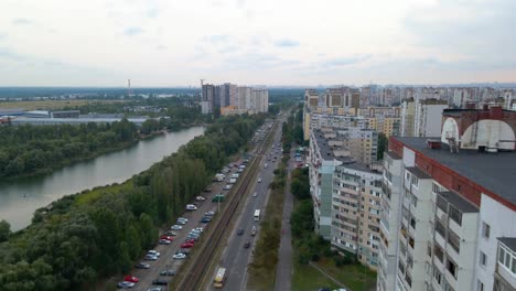 vista aérea del tráfico en una calle, un río y edificios de apartamentos, en un antiguo distrito soviético, día nublado, en la ciudad de kiev, ucrania - carro, tiro de drones