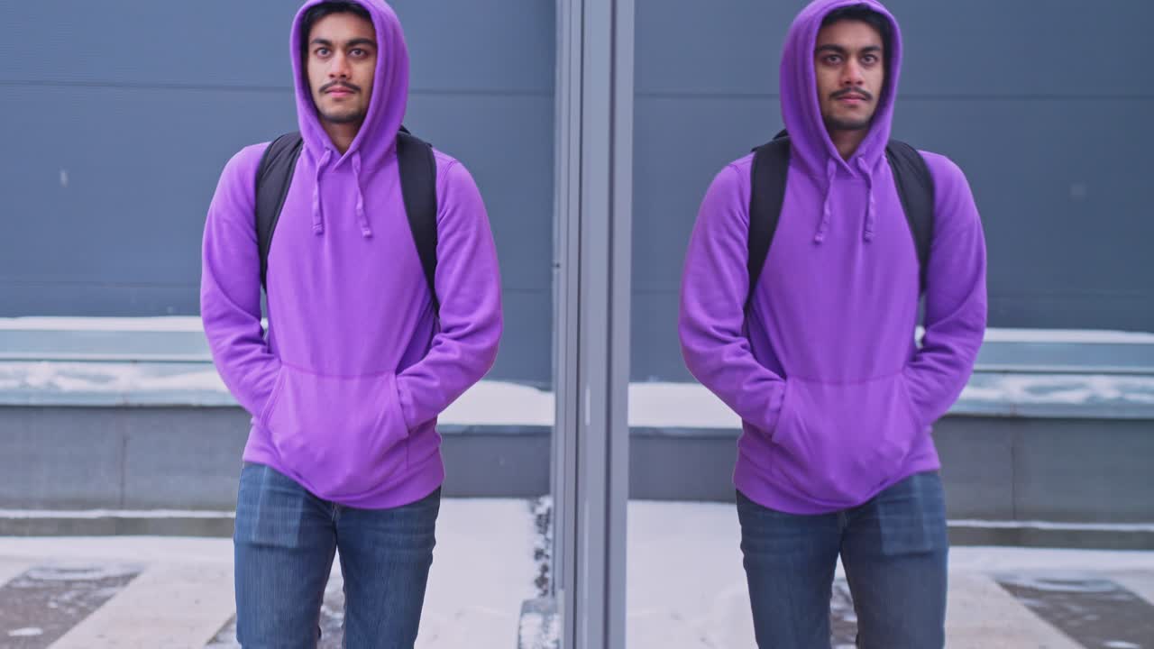 toma en cámara lenta de un hombre vestido con un hoddie morado caminando junto a una ventana de cristal