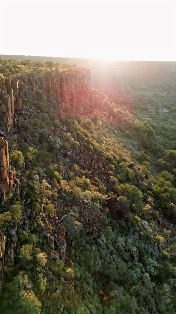 Vista aerea con drone di drammatiche scogliere rocciose e vegetazione verde in Namibia durante la calda luce del tramonto, con vista su una vasta valle selvaggia. Verticale