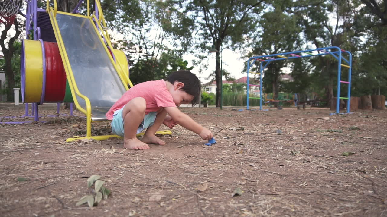 East Asian boy kid having fun playing at a park with toy cars and going down the slider after school