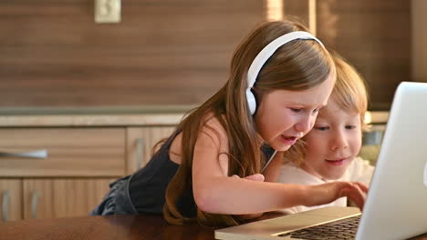 niña y niño emocionados usando una computadora portátil con auriculares inalámbricos y divirtiéndose en casa