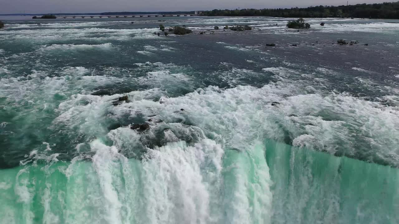 Drone captures close view of waterfall in Canada with turquoise water rushing over rocky edge, forming mist and powerful flow below, creating dramatic and natural scenic landscape from above