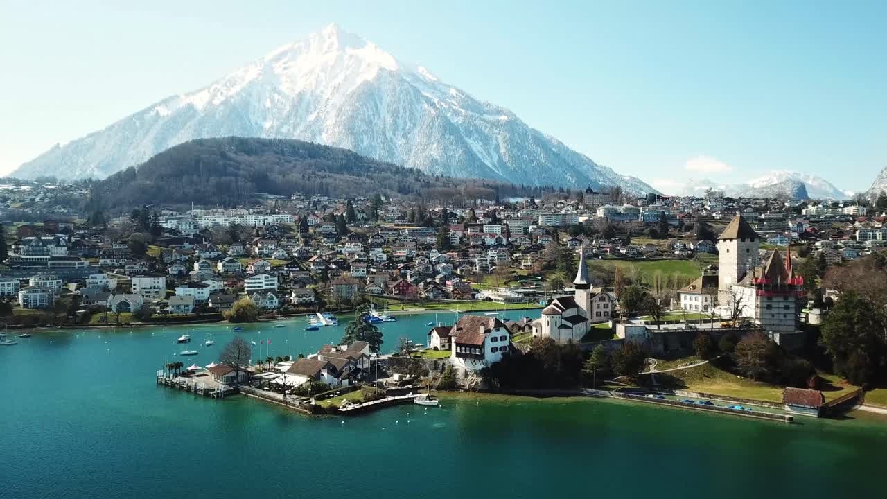 Stunning drone view of Spiez, by the Lake Thun, Switzerland with snowy mountains on the horizon.