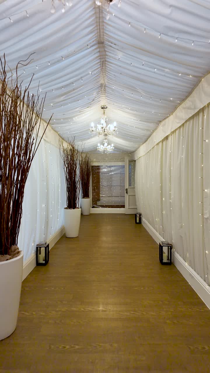 Elegante interno di tunnel tendone per matrimoni con drappeggi bianchi, lampadari e rami marroni in vasi per celebrazioni di eventi e decorazioni per feste. video verticale