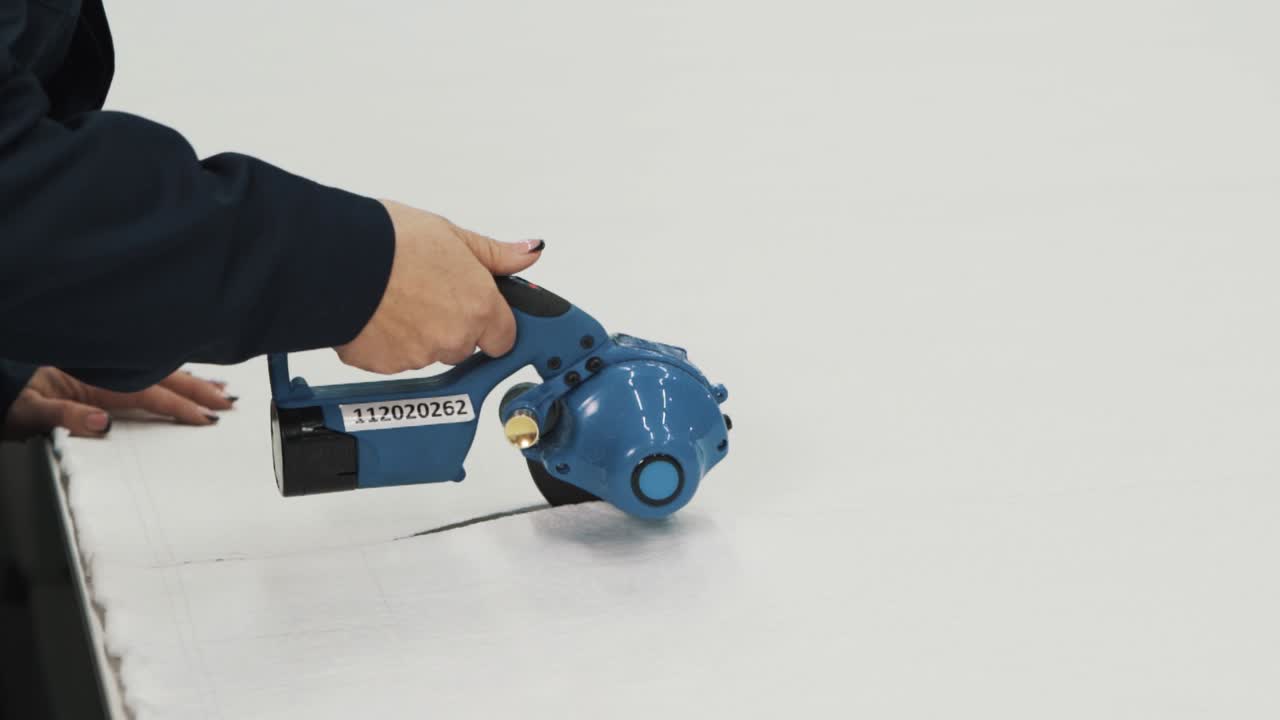 primer plano de manos femeninas cortando tela blanca con tijeras eléctricas de mano en una línea de producción textil