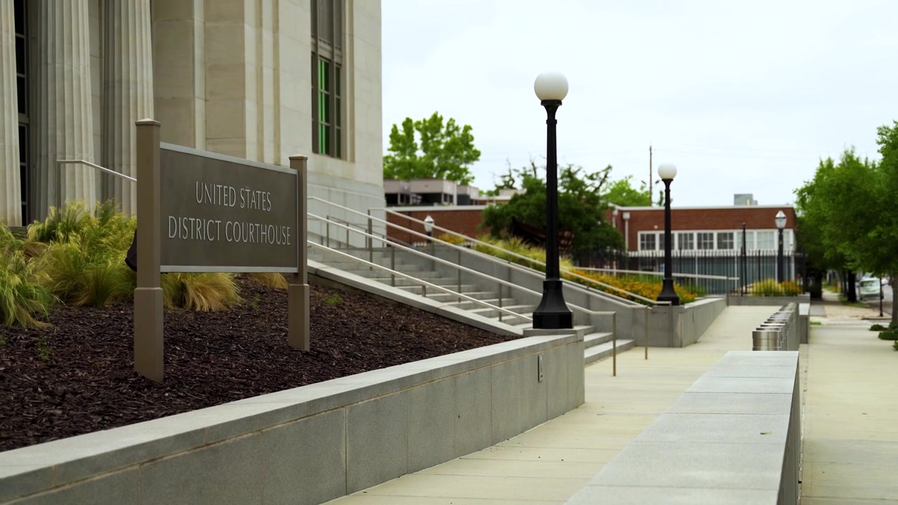 Un'ampia inquadratura stradale dell'insegna del Tribunale Distrettuale degli Stati Uniti a Mobile, Alabama, che mostra grandi scalinate, alte colonne, giardini curati, marciapiedi e un'imponente architettura civica