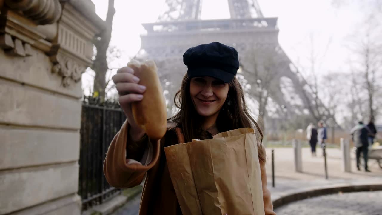 una hermosa mujer europea feliz caminando cerca de la torre eiffel, dando un pedazo de baguette francesa al hombre de la cámara en cámara lenta.