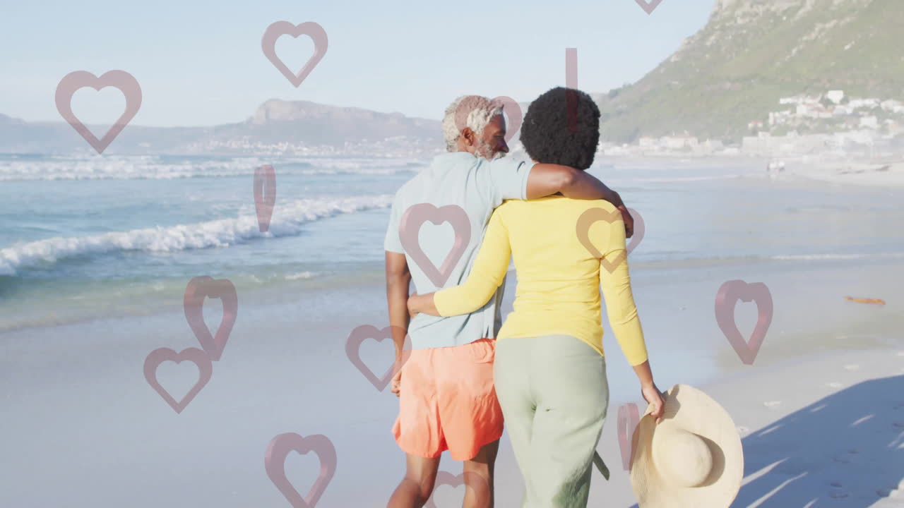 Walking on beach, couple surrounded by heart animations in romantic setting