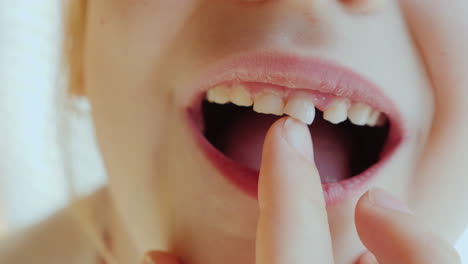 the girl is shaking her finger with a milk tooth which will soon fall out