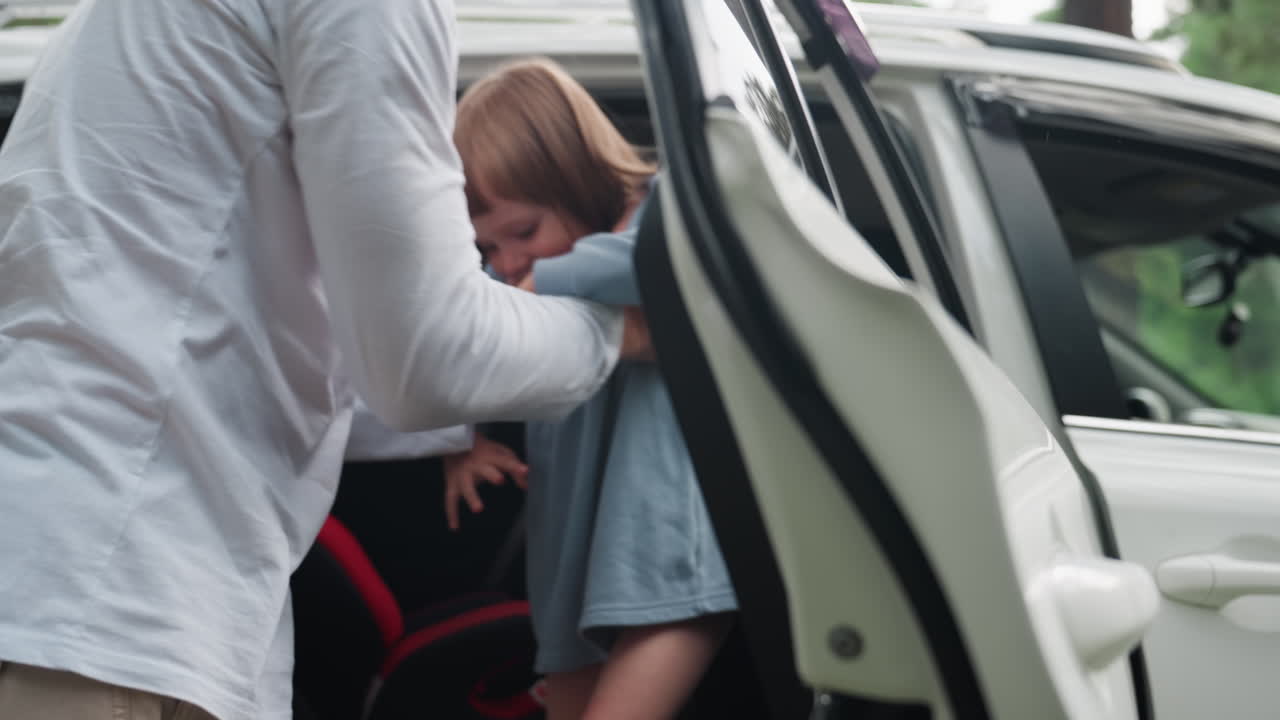 Brother reaches into family suv to carry down younger sister from back seat, open door visible, tender help moment during forest trip, warm sibling care, safe travel routine, candid lifestyle scene