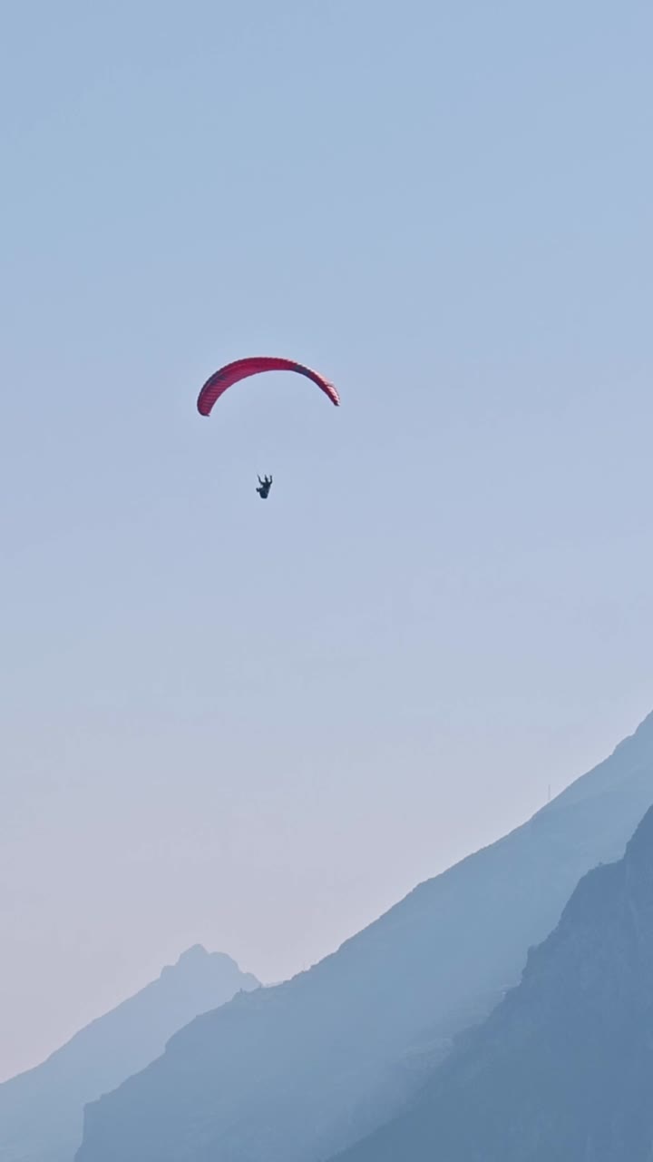 Paraglider pilot flying high over mountain blue haze VERTICAL shot