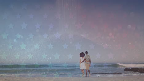 Animation-of-stars-over-back-of-african-american-couple-walking-on-beach