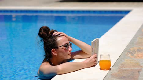la mujer está leyendo un libro junto a la piscina.