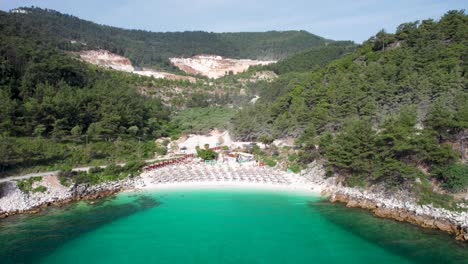 cinematic drone view of marble beach, clear water, white pebbles and lush green vegetation, empty beach, umbrellas, thassos island, greece, mediterranean sea, europe