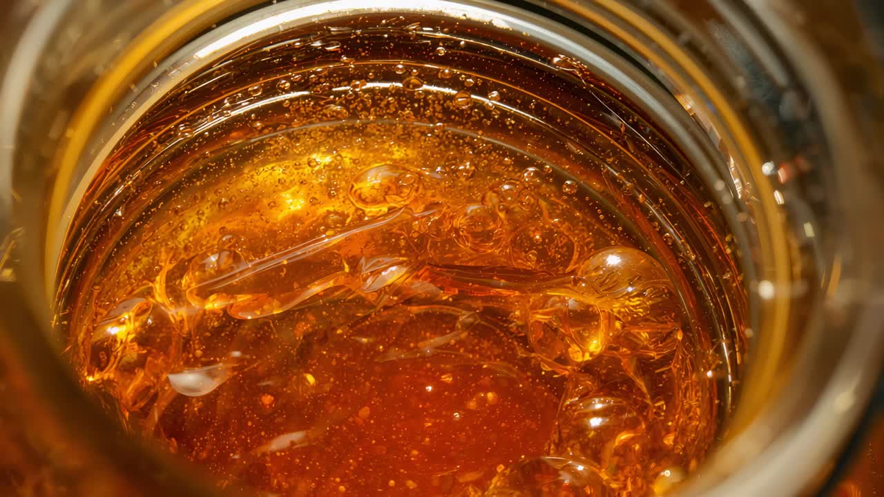Liquido ambrato che si deposita in un barattolo di vetro in cucina dopo essere stato agitato, con bolle che salgono e si uniscono