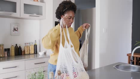 feliz mujer afroamericana desempaquetando compras de comestibles en la cocina, en cámara lenta
