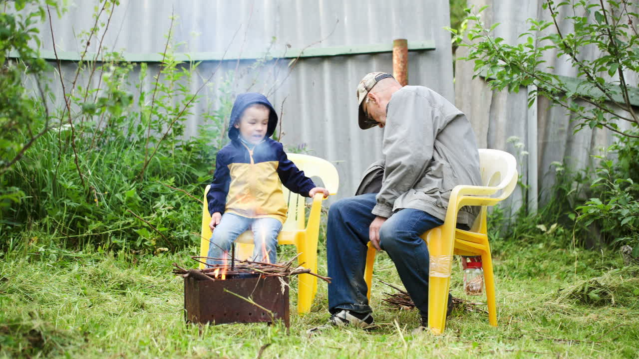 abuelo y su nieto sentados junto al fuego al aire libre