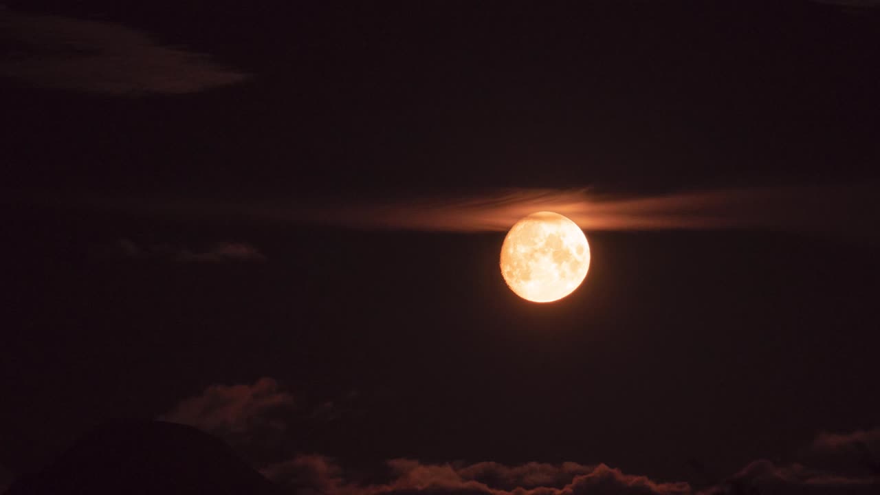 Lindo time-lapse de uma lua dourada flutuando pelo céu noturno, rodeada por nuvens.