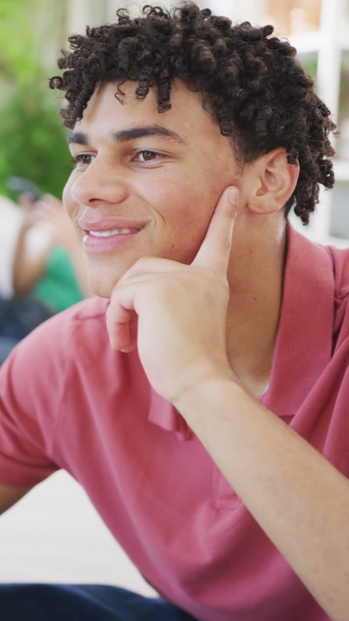 Vertical video of happy biracial man spending time at home and smiling