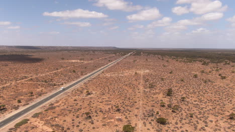 Aerial-drone-panning-shot-of-a-camper-van-on-empty-road-in-barren-environment-on-a-sunny-day