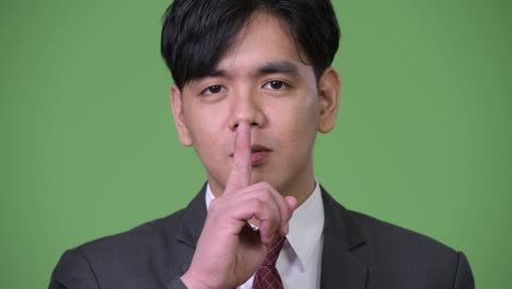 입술에 손가락을 은 젊은 잘생긴 아시아 사업가