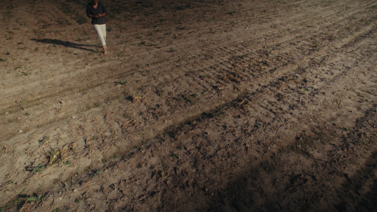 Man Walking Barefoot in a Dry Tilled Field