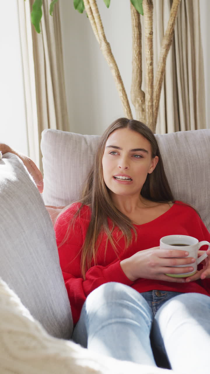 video vertical de una mujer caucásica feliz sentada en el sofá con café