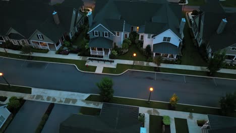 Aerial view of modern American suburban architecture with gabled roofs, chimneys, uniform facades, front porches and landscaped yards during evening twilight. New developed homes in peaceful area