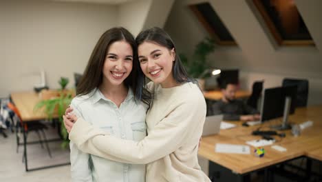 two women hugging and smiling at each other in office