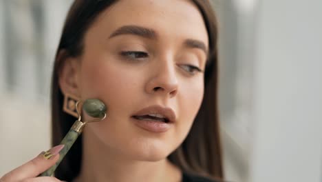 close-up portrait of a young woman massaging her face with a jade roller