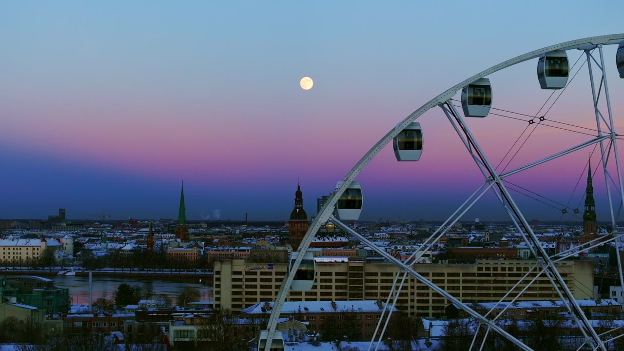 Magical winter evening in Riga with Ferris wheel, moon above snowy skyline